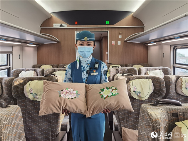 趙瑩靜展示中老鐵路國(guó)際旅客列車(chē)?yán)飵в兄袊?guó)牡丹花和老撾占巴花刺繡圖案的靠墊。人民網(wǎng)記者 杜明明攝