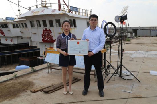 海鮮電商張夢琴與幫辦員手持食品經(jīng)營許可證合影。贛榆區(qū)委宣傳部供圖